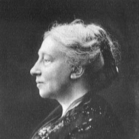 Black and white photograph of Augusta Gregory, shown in profile from the waist up. She is wearing a dark sweater and her light, wavy hair is pulled back.