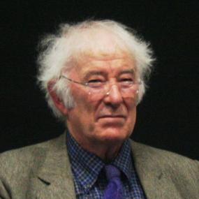 Colour photo of Seamus Heaney taken at University College Dublin, 11 February 2009. He looks ahead, with a weather-beaten face, tousled white hair, and side-burns. He wears rimless glasses, and a tweed jacket over a blue shirt and tie.
