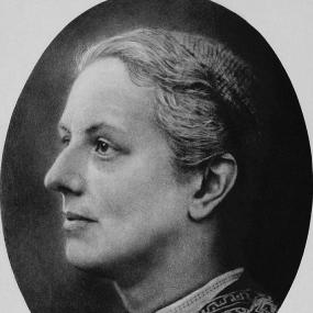 Black and white reproduction of  an albumen print of Charlotte Yonge's head by the Rev. Duke Yonge, 1858? The image is oval; the sitter is seen in profile facing left. She is wearing a small, light cap, a pale ribbon around her neck fastened with a brooch (perhaps a cameo), and embroidery around her collar. National Portrait Gallery.